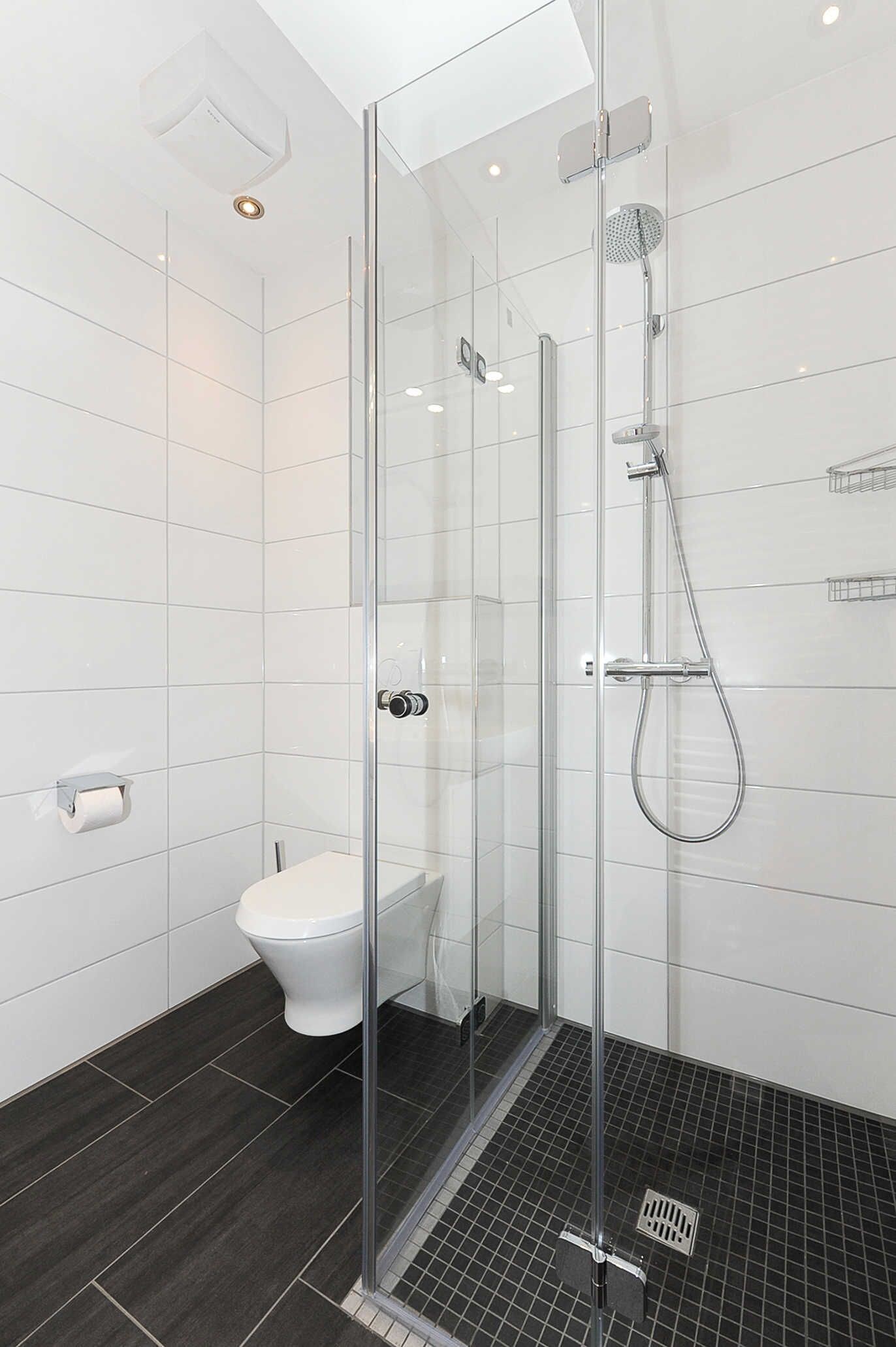 Un bagno moderno con doccia vetrata, un water e un pavimento piastrellato scuro.
