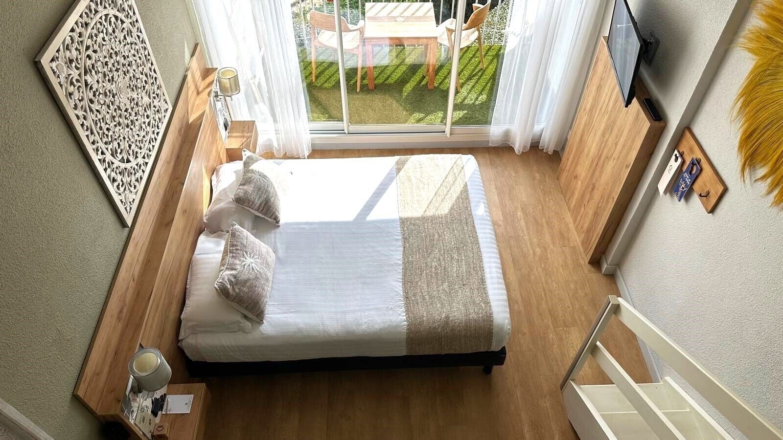 Un dormitorio con cama, mesita de noche, televisor y vista a un patio exterior.