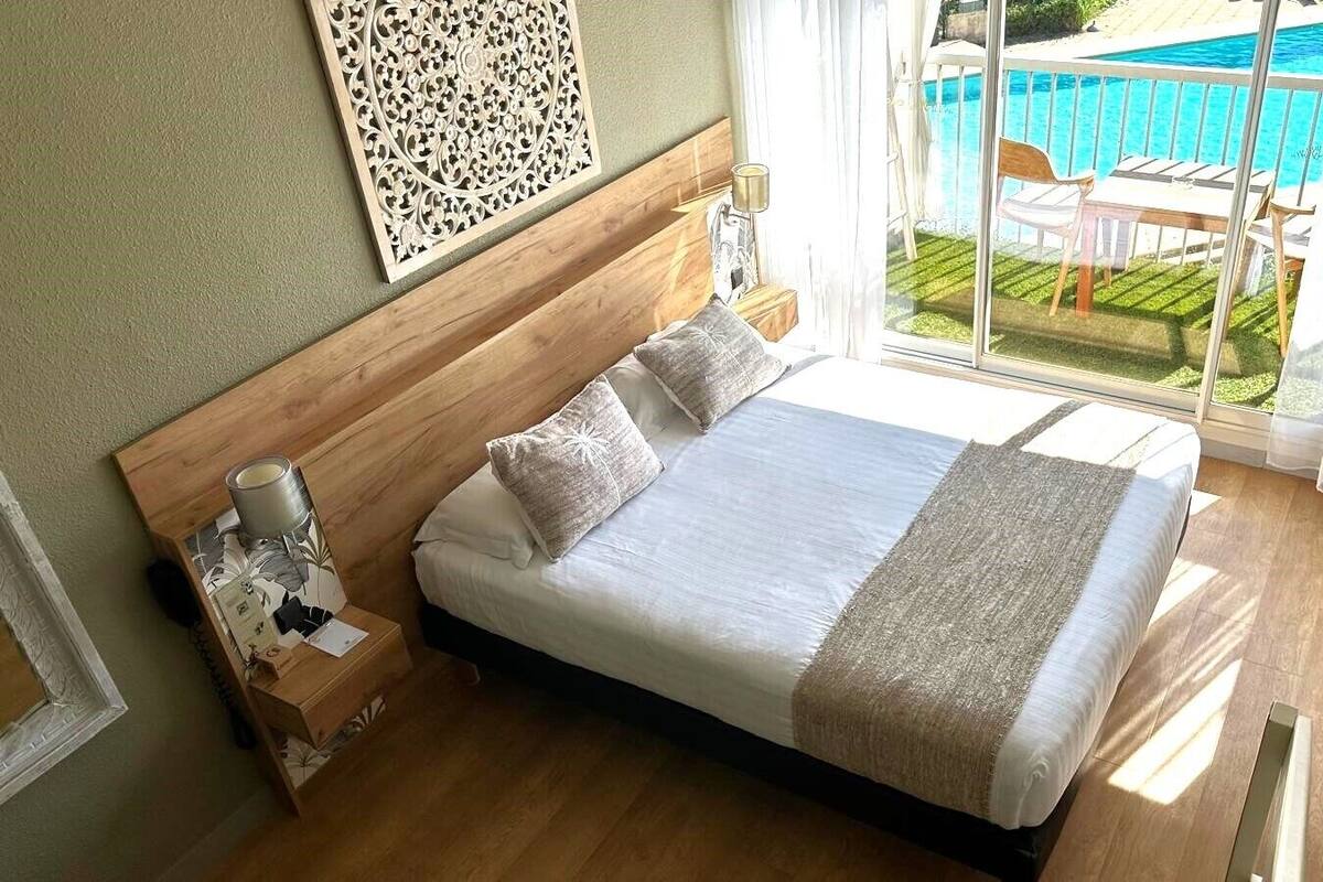 A bedroom with a large bed, a nightstand, a lamp, and a view of a swimming pool.