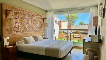Une chambre avec un grand lit, une tête de lit en bois ornée de motifs complexes, un bureau avec une chaise et une vue sur le balcon extérieur.