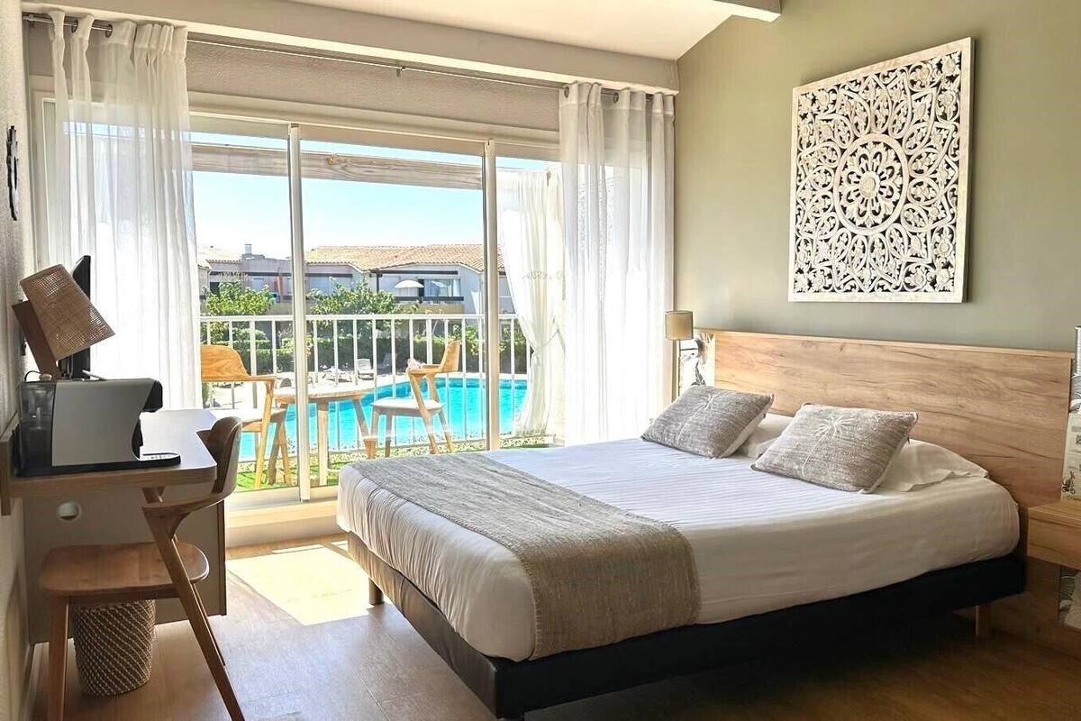 A bedroom with a large bed, a desk, and a view of a swimming pool.