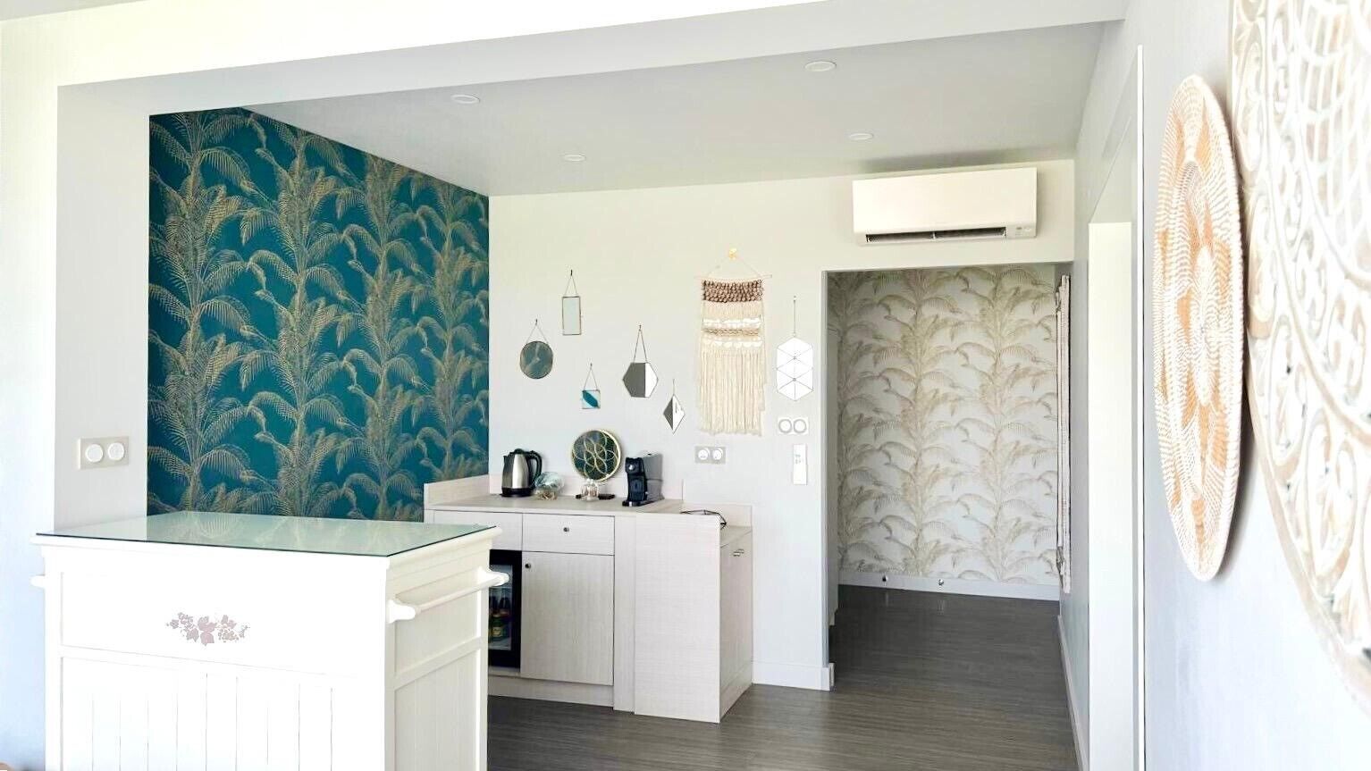 Een kleine keuken met witte kastjes, een kookeiland met glazen blad en decoratieve wanddecoraties.