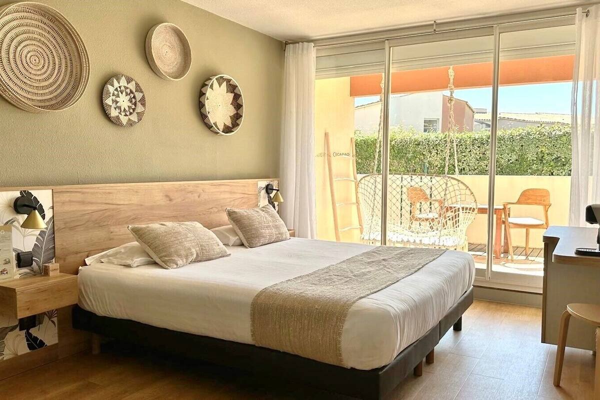 A bedroom with a bed, bedside table, lamp, and a view of the outside balcony.