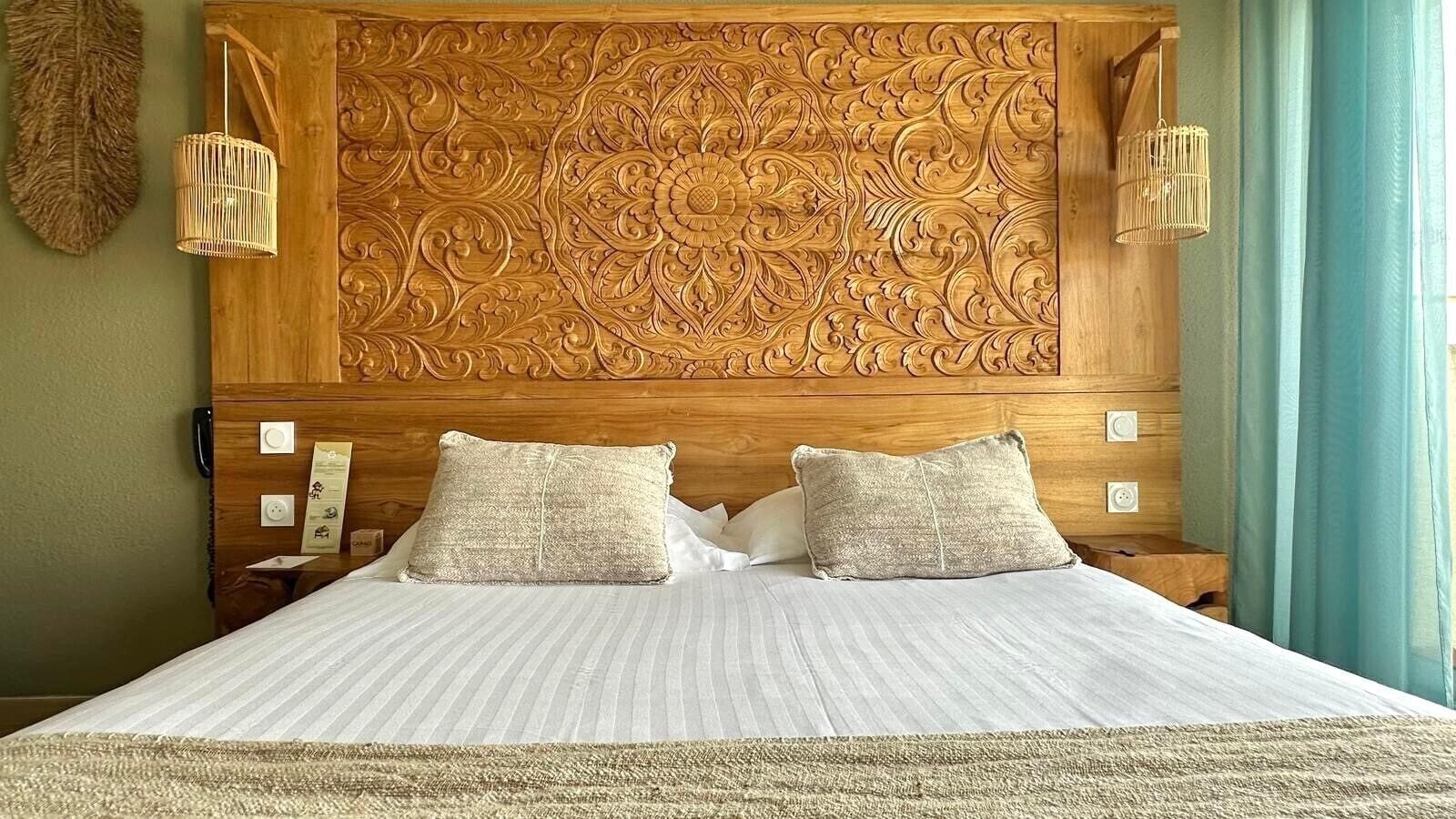 A bed with a wooden headboard featuring intricate carvings, two bedside tables with lamps, and a textured rug.