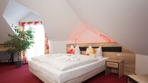 A bedroom with a bed, bedside table, nightstand, and a potted plant. - Hotel 3 Linden (Leipzig)