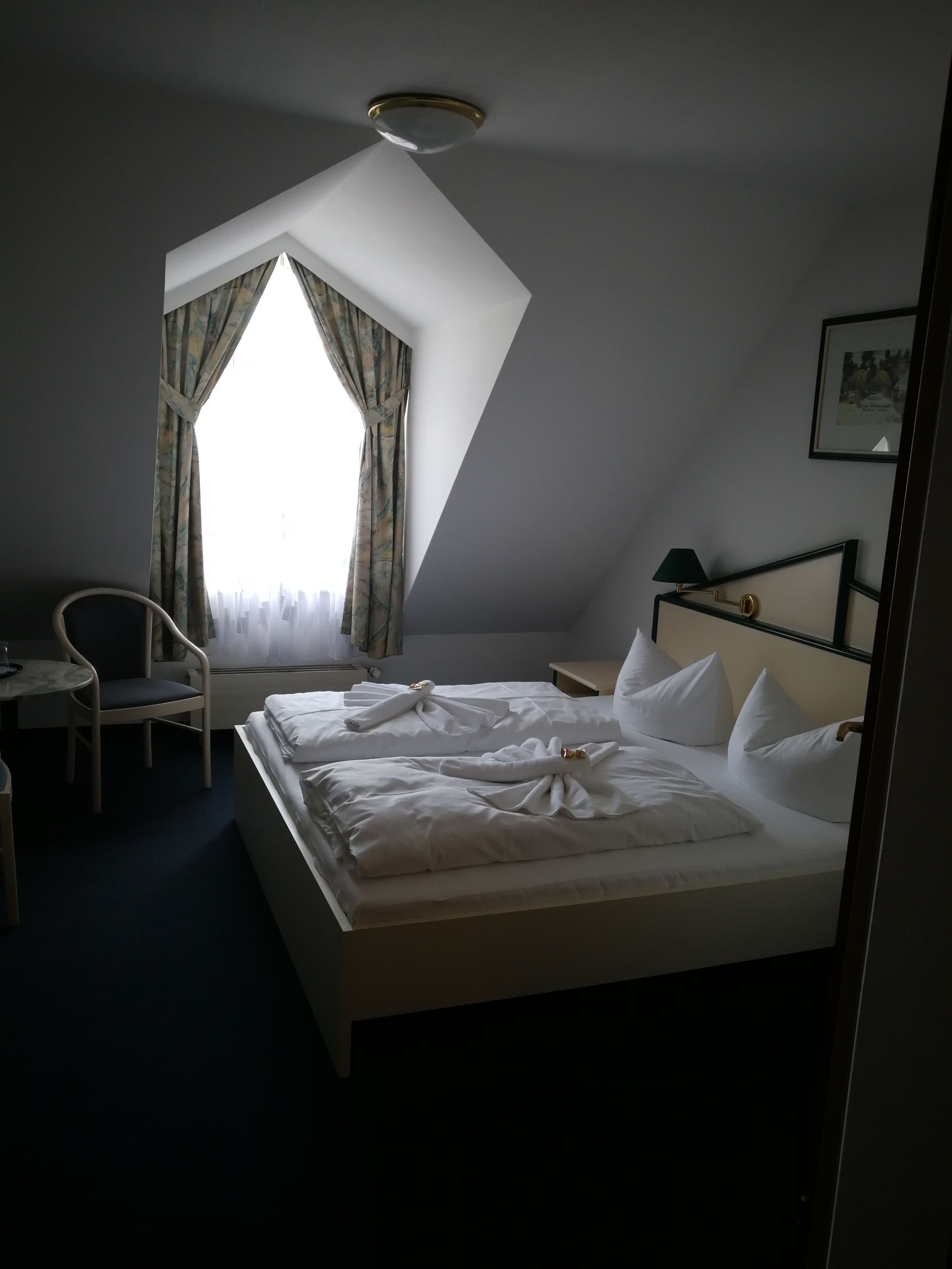 Een hotelkamer met een bed, een stoel, een bureau en een raam met gordijnen.