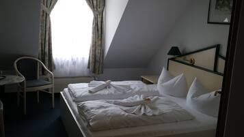A hotel room with a bed, a chair, a desk, and a window with curtains.