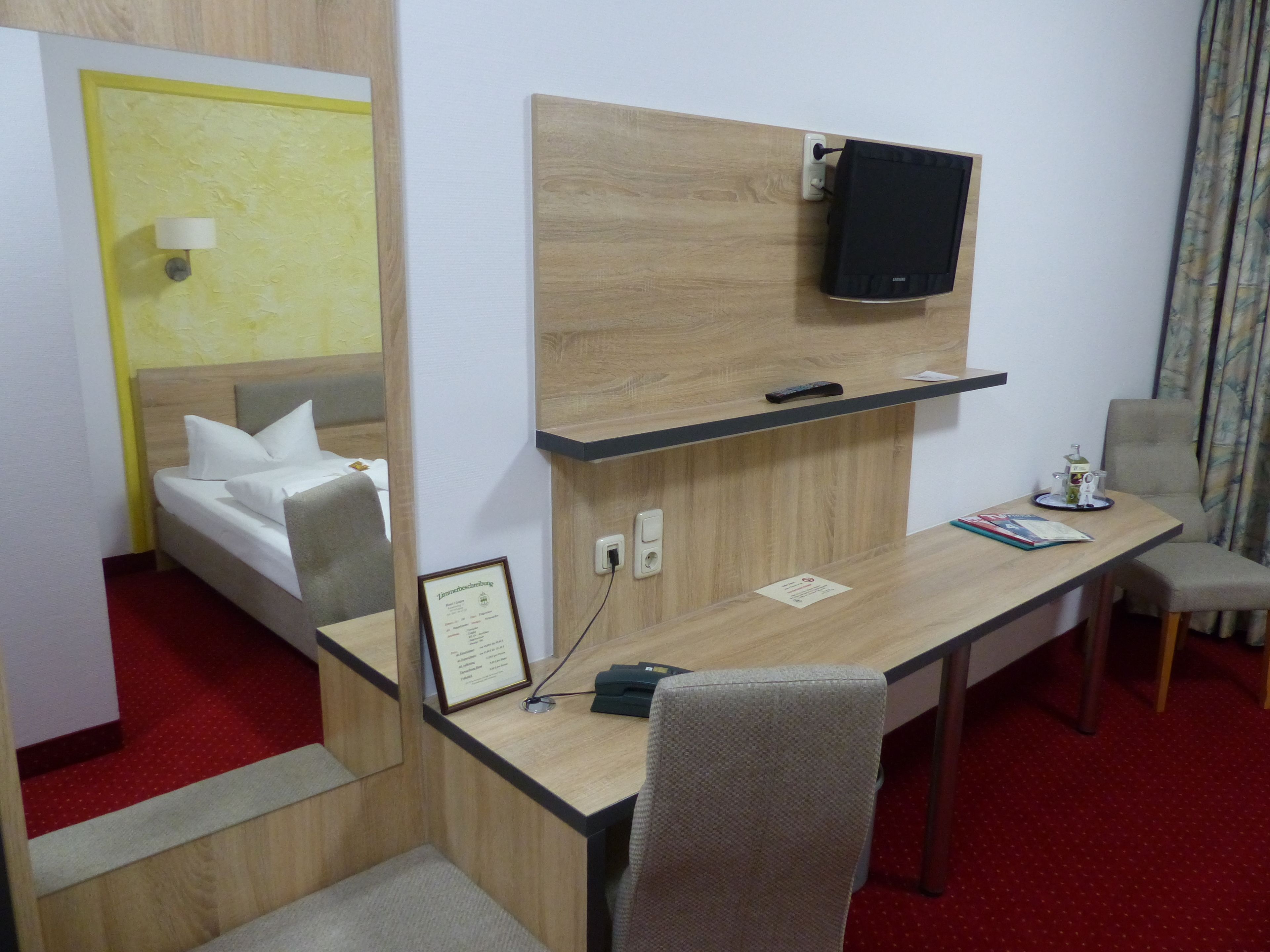 A hotel room with a bed, a desk, a chair, a television, and a mirror.