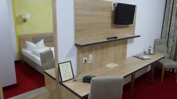 A hotel room with a bed, a desk, a chair, a television, and a mirror.