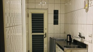 A kitchen with white tiled walls, a black and white checkered floor, a stainless steel sink, and a door with horizontal slats. - Orange House B&B Juifen (New Taipei City)