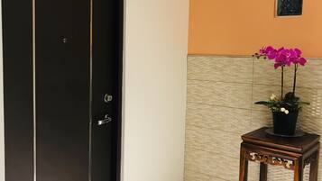 Hotelkamer met een zwarte deur waarop 'B' en '3F' staan, een klein houten tafeltje met een potorkidee en een betegelde vloer.