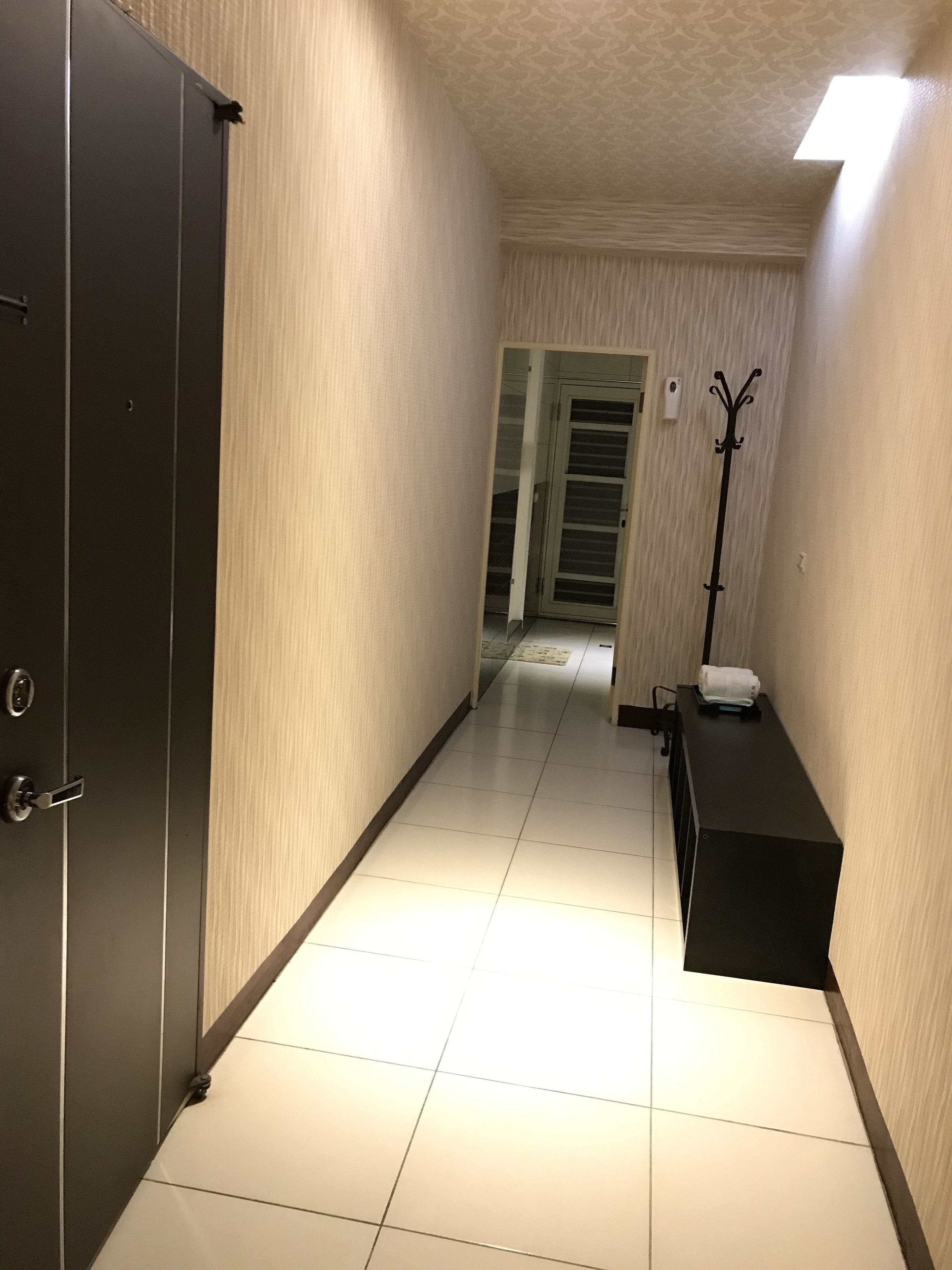 A hallway with a door on the left, a coat rack on the right, and a door at the end.