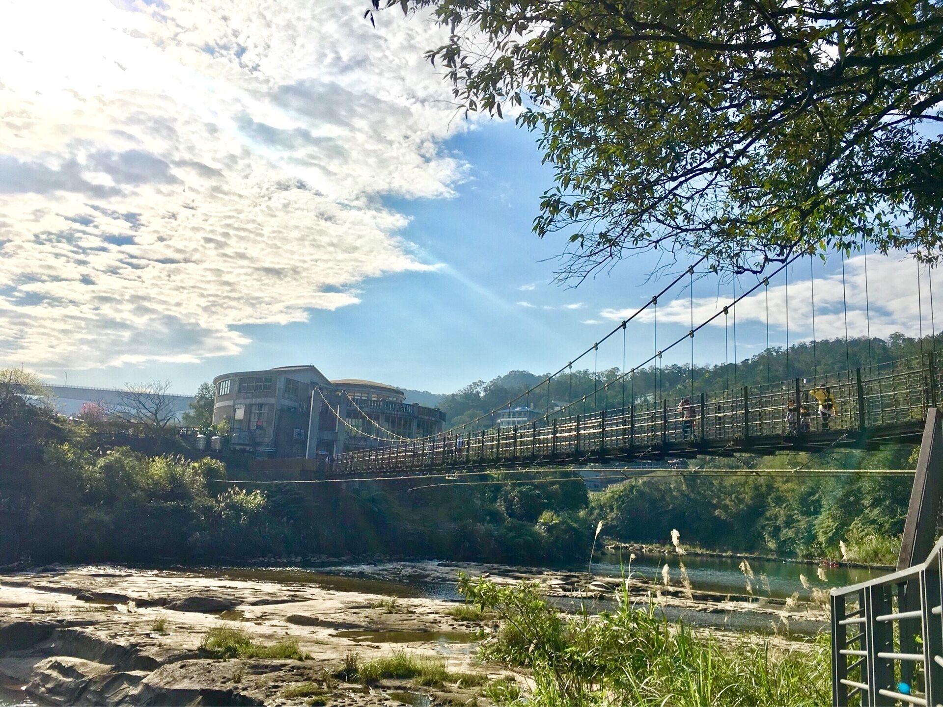 A suspension bridge over a river with a building in the background.