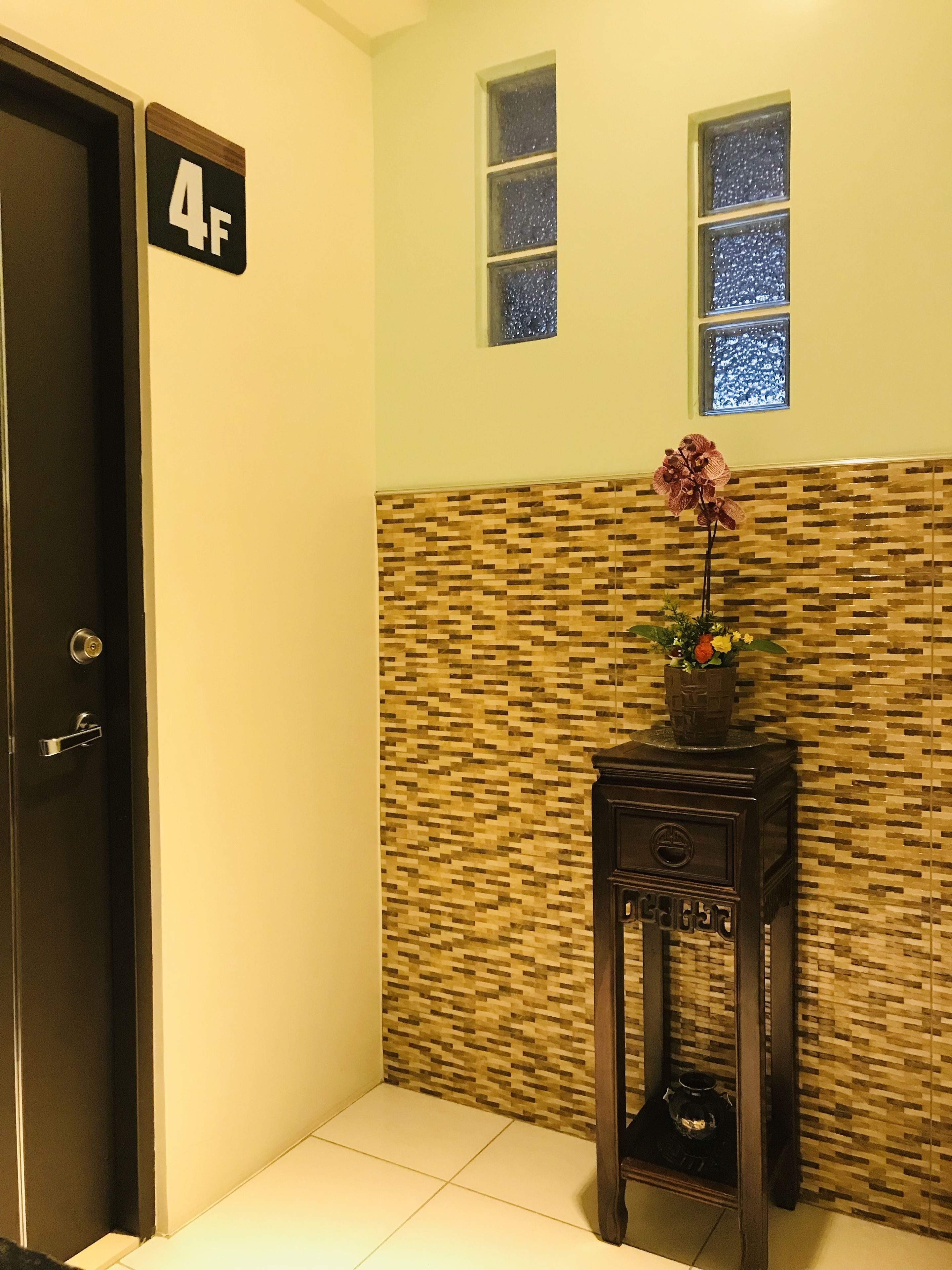 Habitación de hotel con piso de baldosas, una puerta con la etiqueta '4F', una pared con diseño de mosaico y una pequeña mesa con un florero.