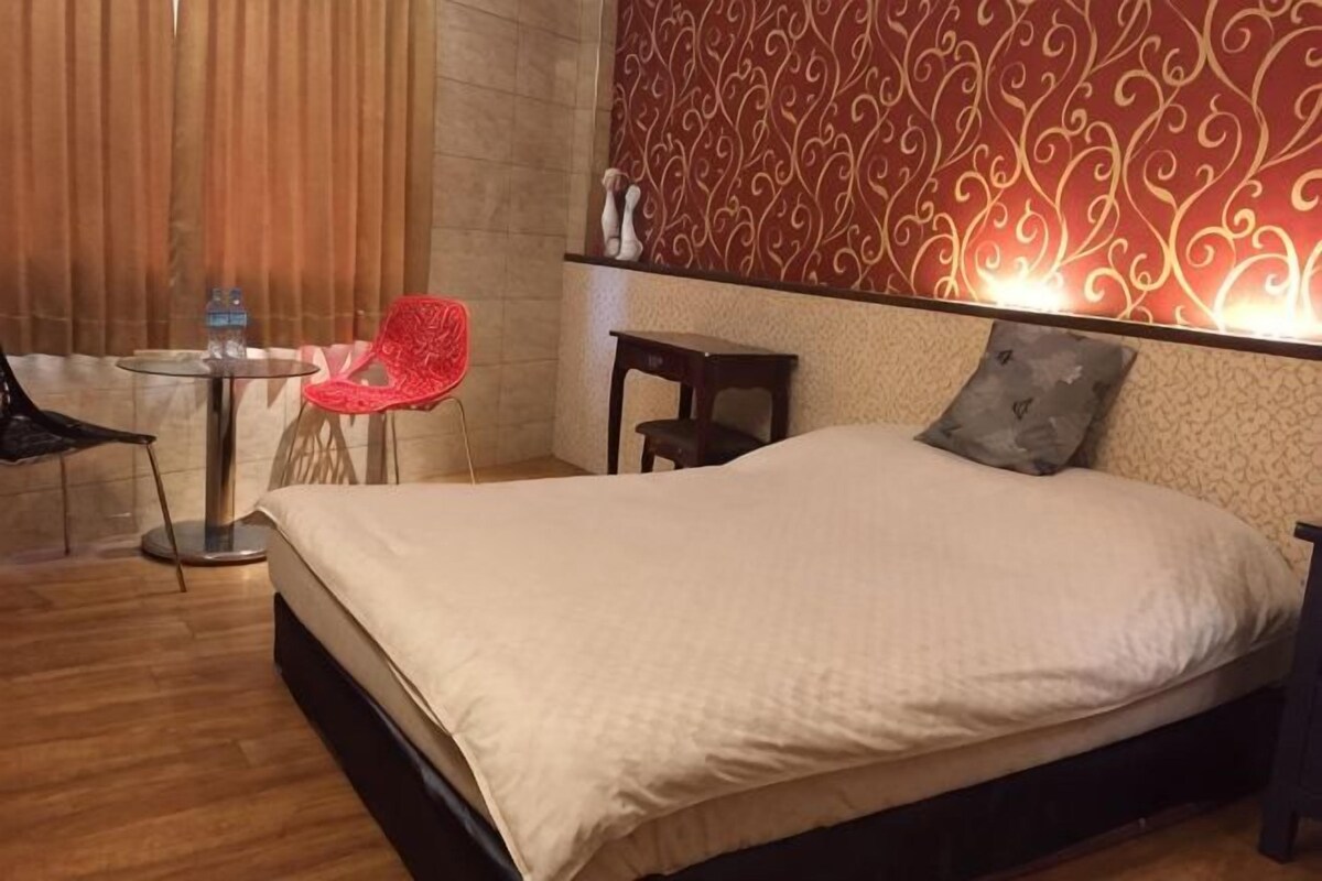 A hotel room with a bed, a small table with a chair, and a decorative wall.