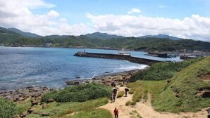 A coastal path with a rocky shoreline, a pier extending into the water, and mountains in the background. - Orange House B&B Juifen (New Taipei City)