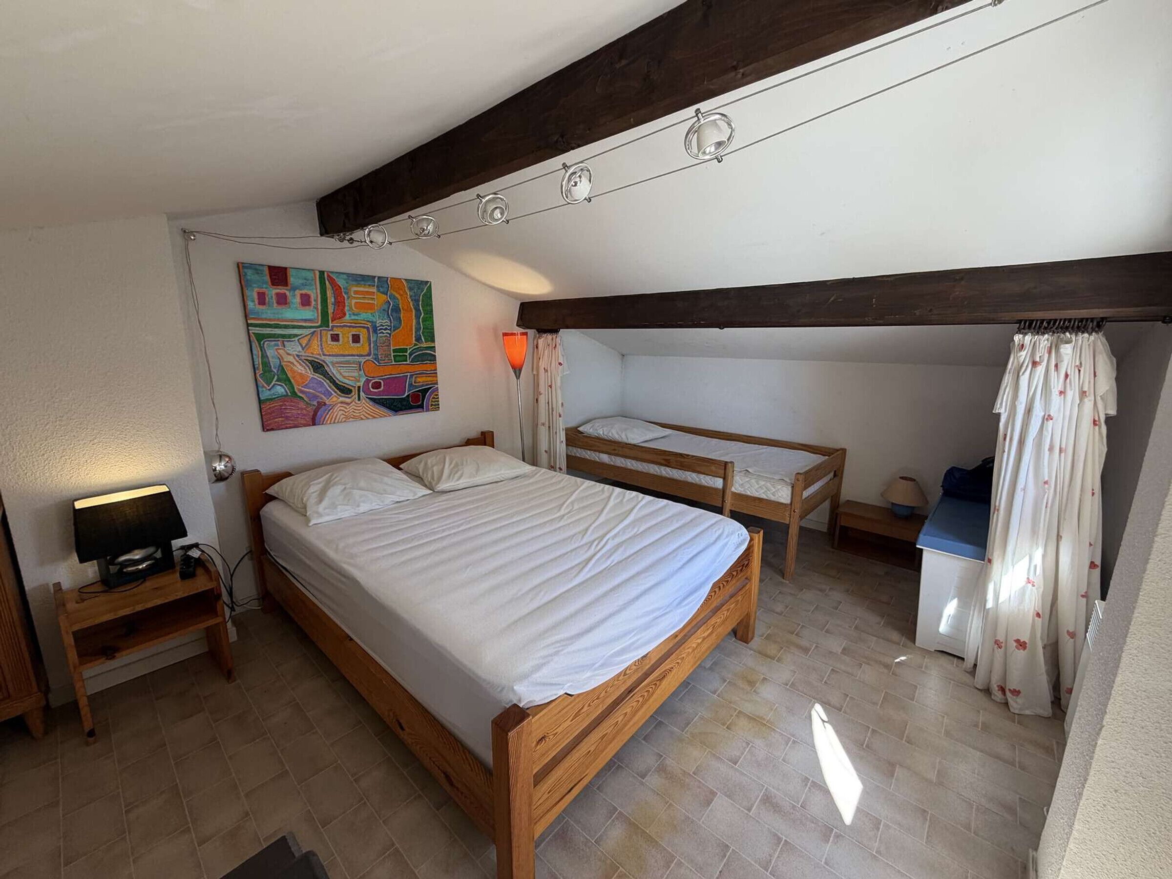 Une chambre à coucher avec un lit, une table de chevet, une lampe et un tableau coloré au mur.
