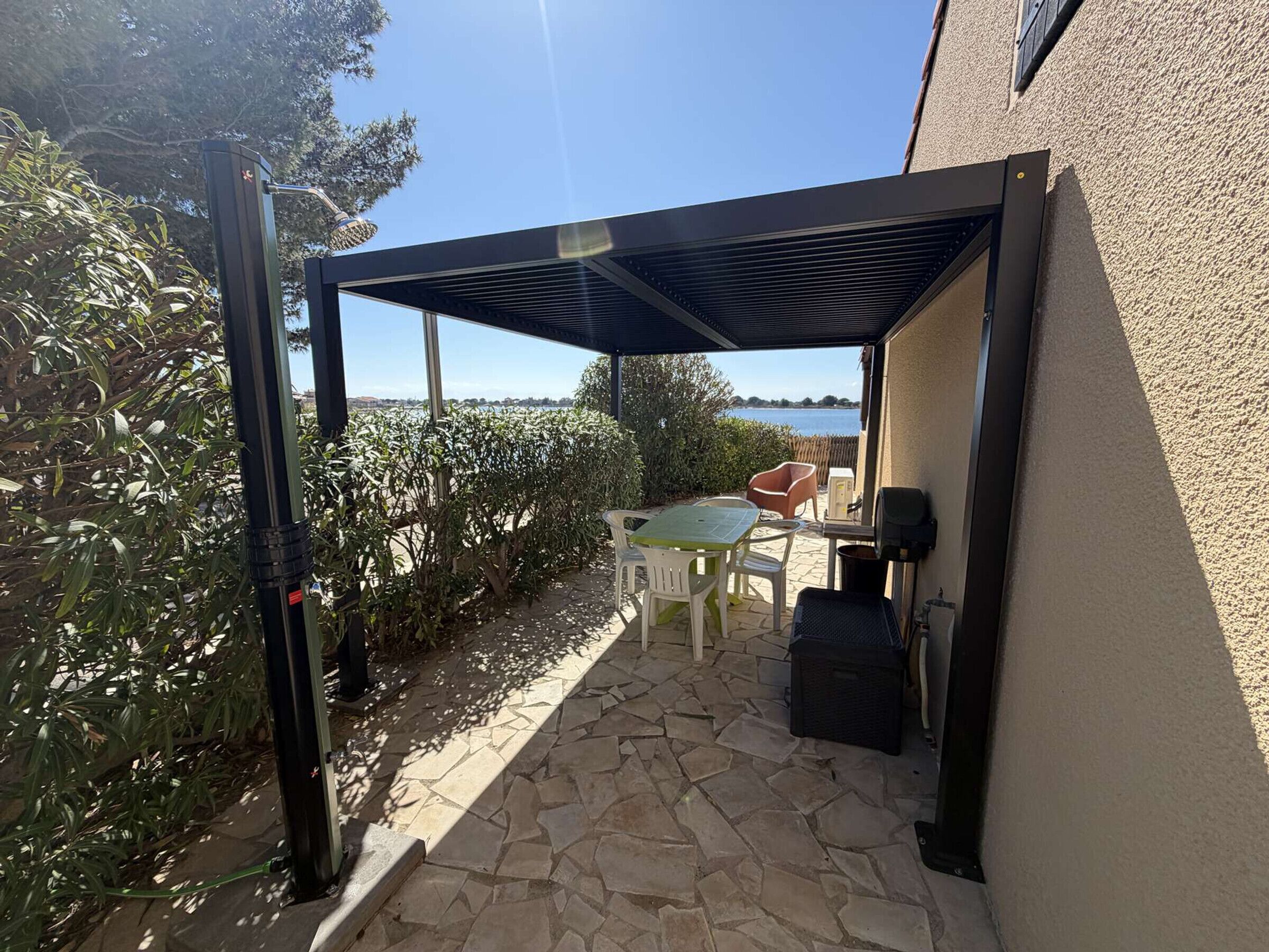 A covered patio with a table and chairs, a trash bin, and a view of the water.