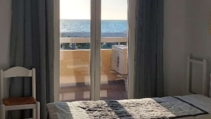 Una stanza con un letto, una sedia e una porta scorrevole in vetro che dà su un balcone con vista sul mare.