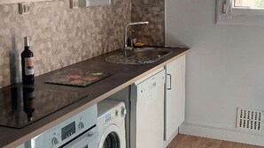 Una cucina compatta con lavatrice integrata, una bottiglia di vino e una finestra vista verde.
