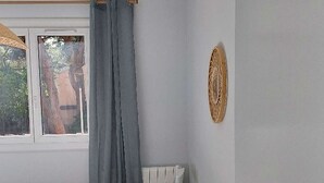 Una camera da letto con un letto, una sedia, una finestra con tende e un elemento decorativo a parete.