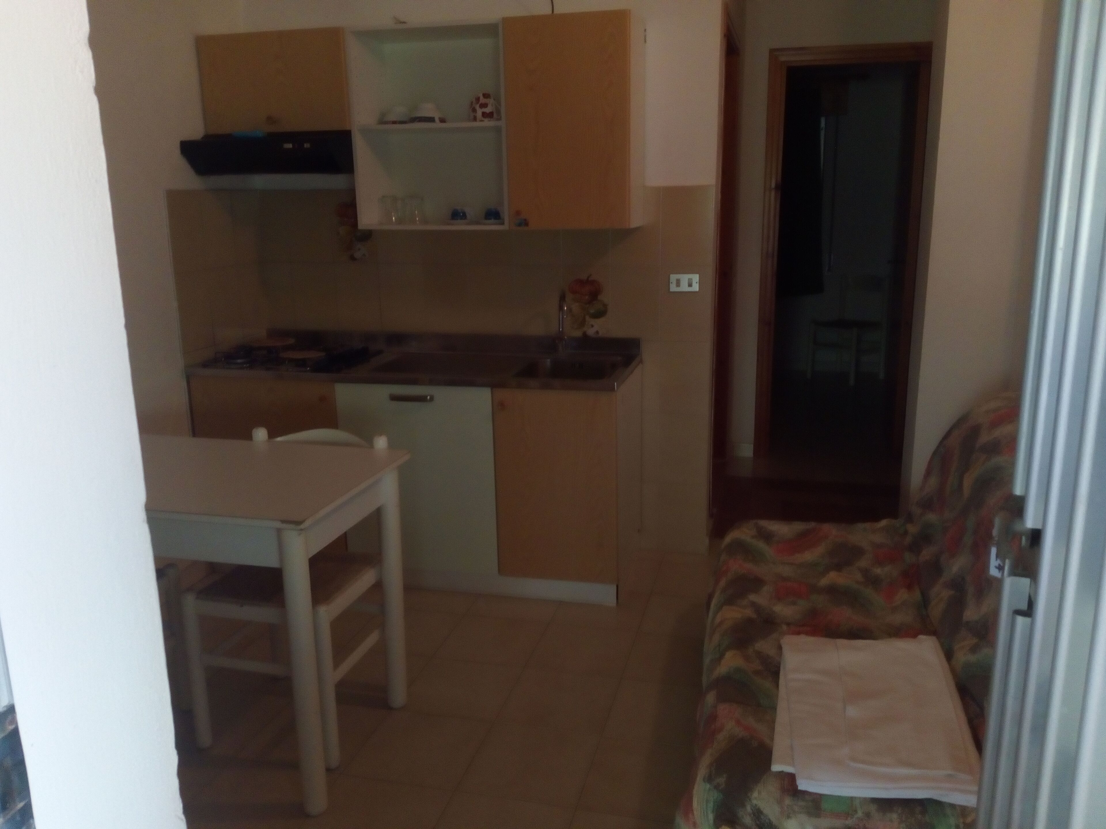 A compact kitchen with a dining table and chairs, a sofa with a blanket, and a door leading to another room.