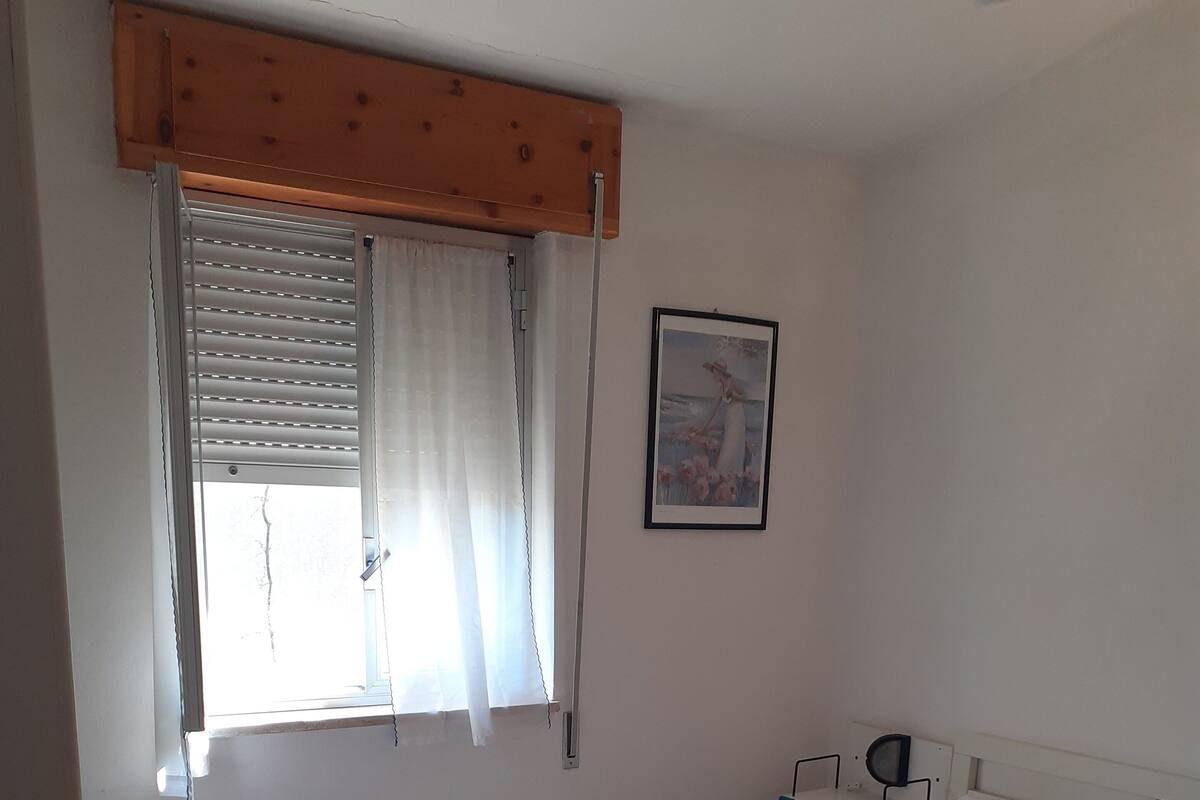 A bedroom with a single bed, a window with blinds, a wall-mounted picture, and a tiled floor.