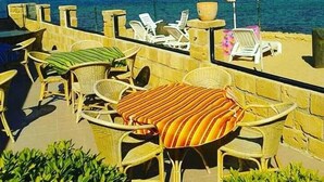 Une terrasse en bord de mer, avec des chaises en osier et une nappe à rayures, offrant une vue sur la mer.