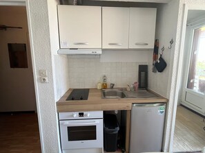 A compact kitchen with white cabinets, a sink, a stove, and a refrigerator.