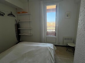 A small, clean room with a bed, a chair, a window with a view of a building, and a door.