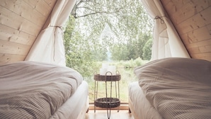 A cozy tent with two beds, a small table with candles, and a view of greenery outside. - Sju Sjöar Konferens (Oxnevalla)