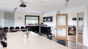 Une cuisine moderne dotée d’une grande fenêtre, un coin repas avec une longue table et des chaises, et un espace détente avec des fauteuils en osier.