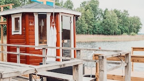 A wooden cabin with a dock extending into a body of water, surrounded by trees. - Sju Sjöar Konferens (Oxnevalla)