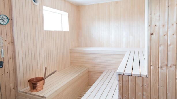 A sauna room with wooden walls and benches, a small window, and a copper bucket. - Sju Sjöar Konferens (Oxnevalla)
