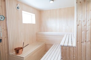 A sauna room with wooden walls and benches, a small window, and a copper bucket. - Sju Sjöar Konferens (Oxnevalla)