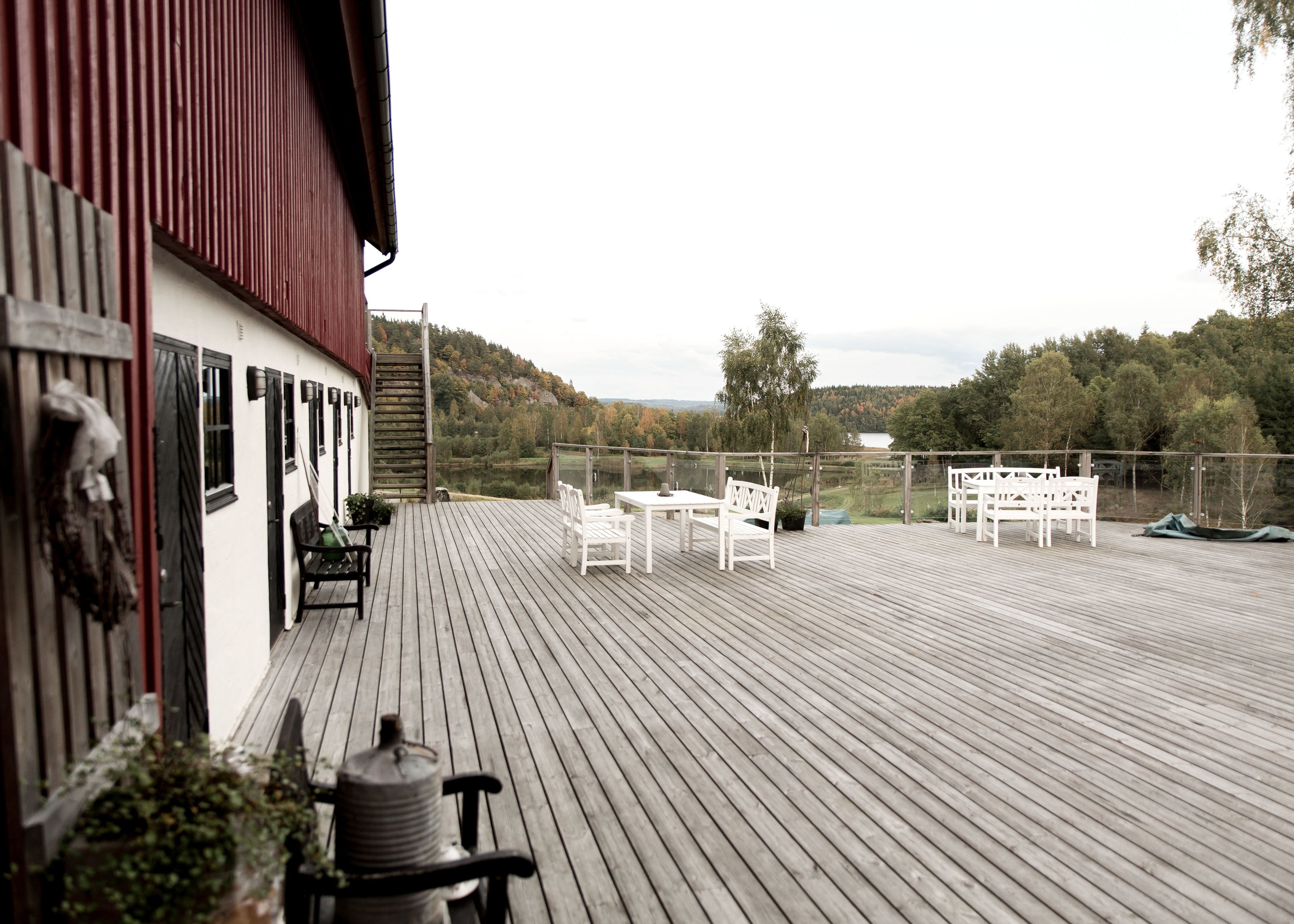 A wooden deck with outdoor seating and a view of a lake and forest.