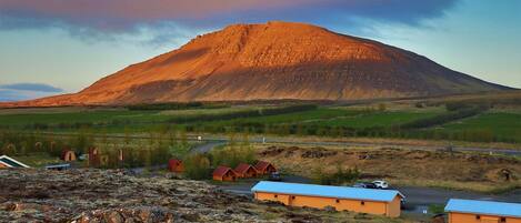 A mountain with a flat top, surrounded by green fields and a few buildings with red roofs.