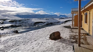 A wooden building with a deck overlooking a snowy landscape and a river. - Fossatún Country Hotel (Borgarbyggd)