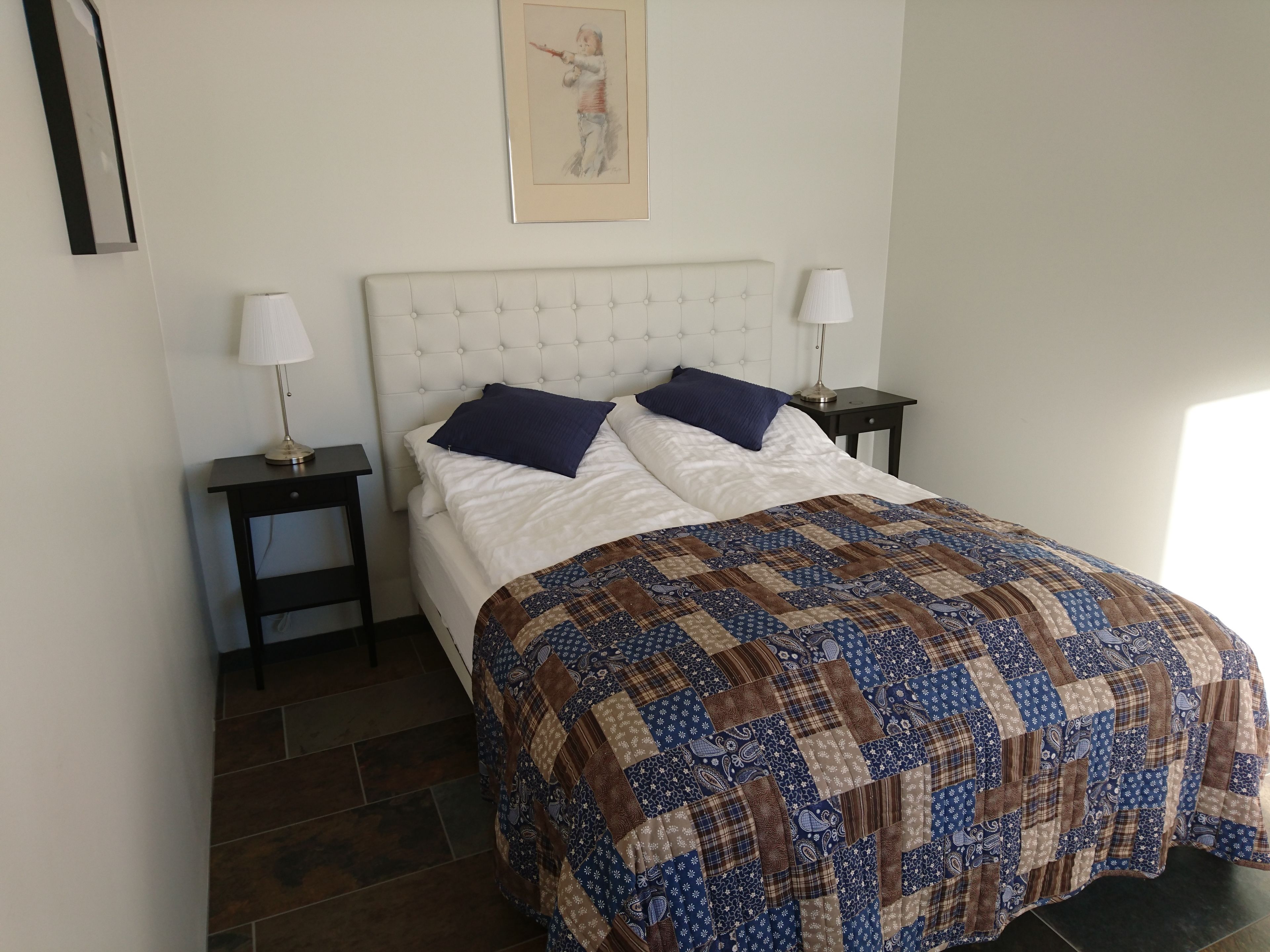 A bedroom with a white bed, two nightstands, a quilt, and a framed picture on the wall.