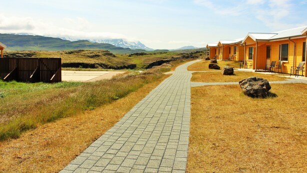 A pathway leading to a row of wooden cabins with a mountainous backdrop. - Fossatún Country Hotel (Borgarbyggd)