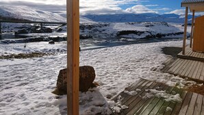A wooden deck with a view of snow-covered mountains and a bridge in the distance. - Fossatún Country Hotel (Borgarbyggd)