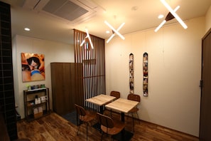 A dining area with a wooden table and chairs, a shelf with kitchenware, and a wall-mounted picture.