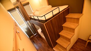 Quarto compacto com escada de madeira, cama pequena com colchão e um banco de madeira.