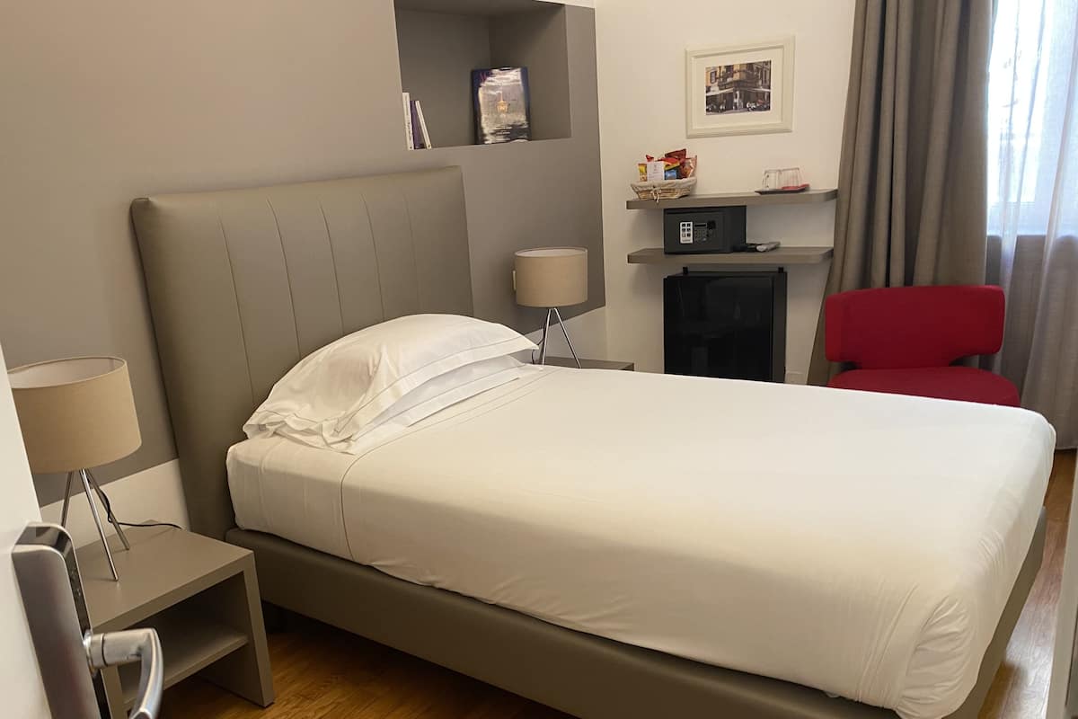 A modern hotel room with a large bed, a bedside table with a lamp, a red chair, and a fireplace.
