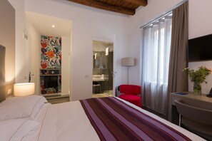 Habitación de hotel con cama, escritorio, silla, televisión y baño visible a través de una puerta abierta.
