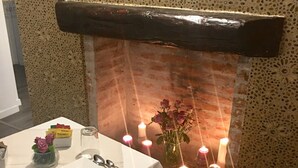 Un coin repas avec une table dressée pour deux personnes, un vase rempli de fleurs et des bougies disposées sur un mur.