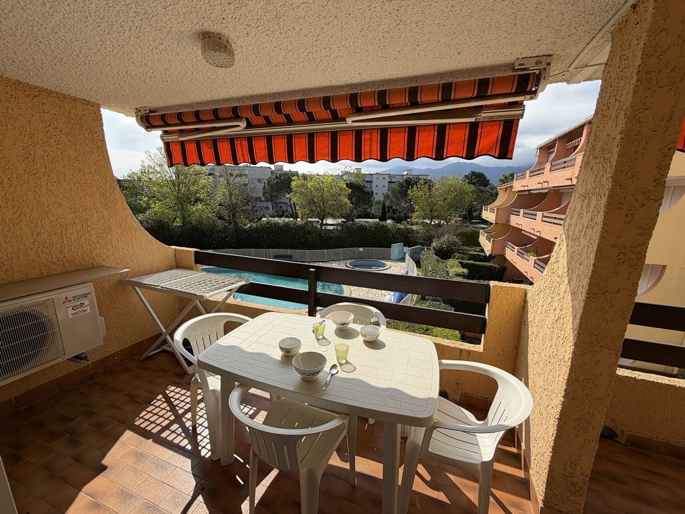 A balcony with a table and chairs, a pool, and a view of buildings and trees.