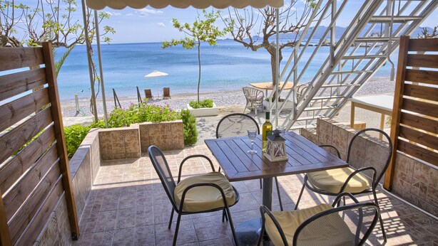 Une terrasse extérieure avec une table et des chaises, une clôture en bois et une vue sur la mer.