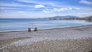 Une plage de galets, deux chaises en bois et un parasol.