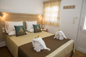 A hotel room with a bed, pillows, a window with curtains, and a wall-mounted light fixture. - Haraki Dream View (Rhodes)